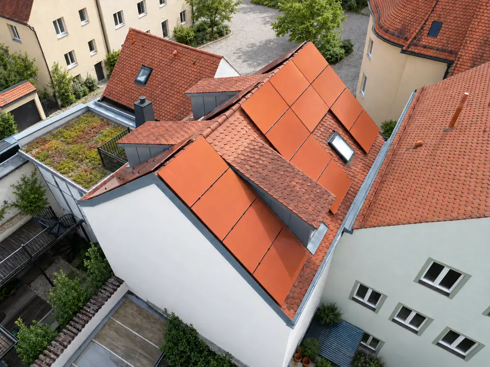 Aus der Luft fotografierte Denkmalschutz-Photovoltaikanlage mit roten Modulen auf mehreren Dachflächen
